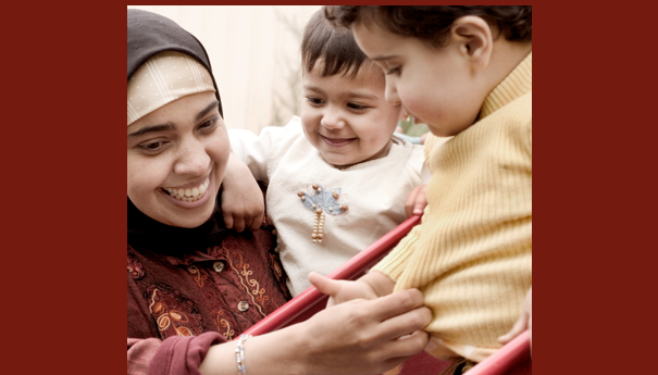 Bilde av en dame som holder et barn i armen, mens hun hjelper et annet på en sklie