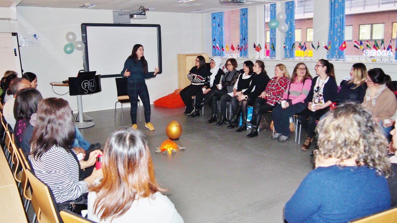 Foto: Mennesker sitter på stoler i ring, en står midten og forteller.